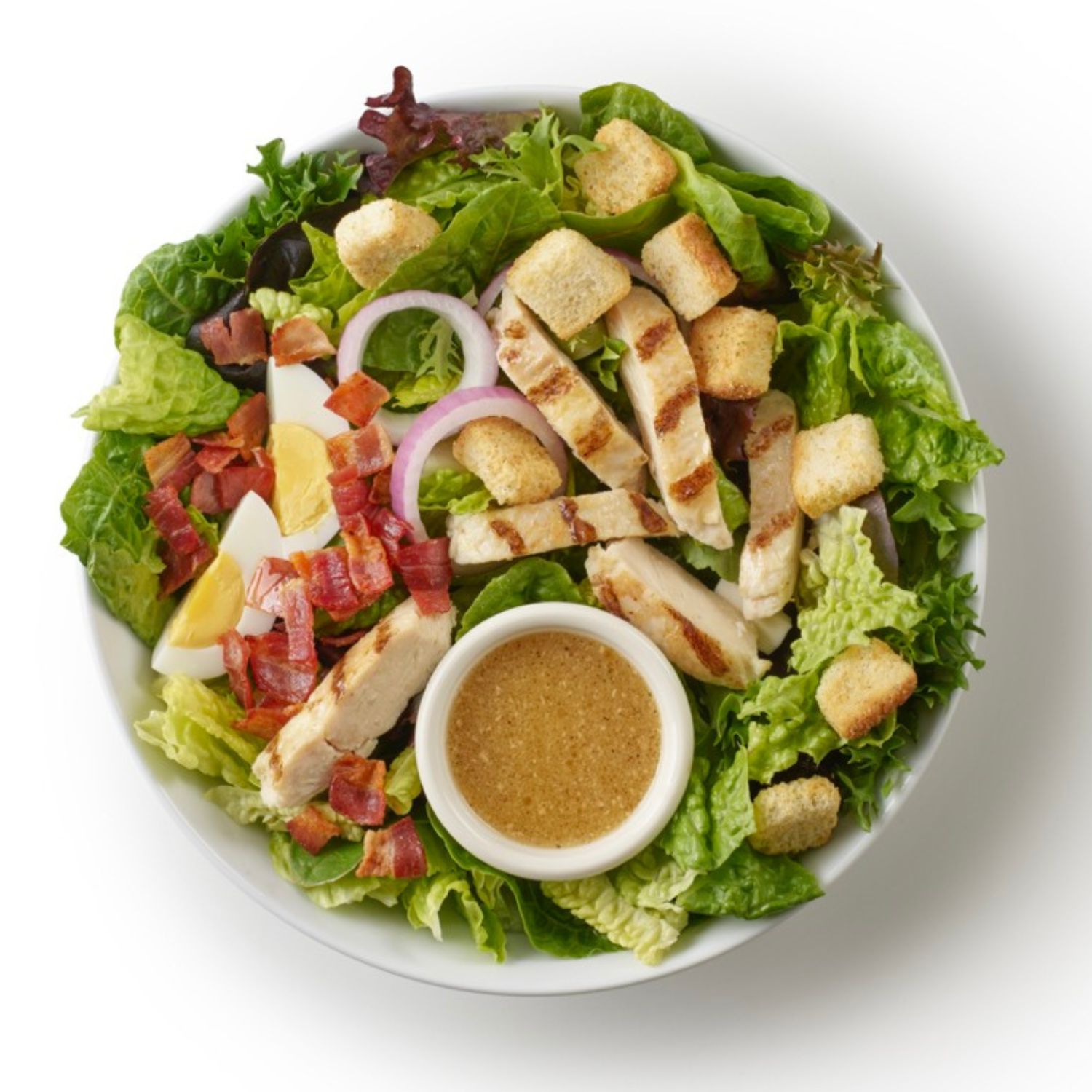 Top-down view of a chicken Caesar salad with romaine lettuce, grilled chicken, bacon, croutons, red onion, egg, and Caesar dressing.